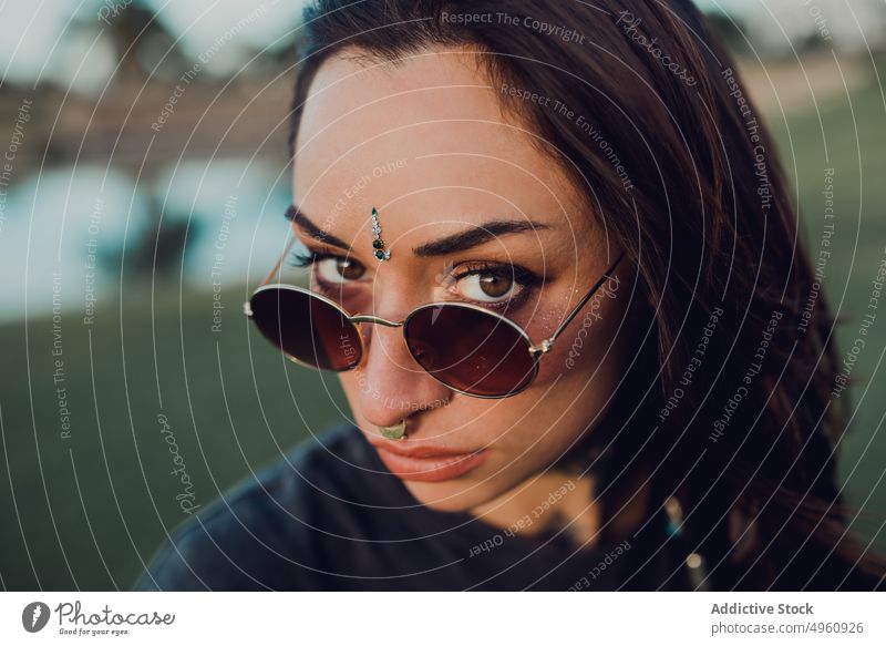 Magnificent trendy adult woman in sunglasses eye gaze bindi cool tattoo appearance rebel eyelashes jewelry brunette fashion female tradition allure personality