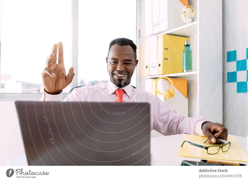 Glad black businessman having video call on laptop in office greeting smile masculine professional independent using gadget device netbook gesture show