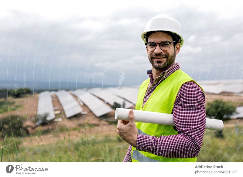 Positive man with blueprint standing near solar farm engineer power station draft smile positive work countryside male professional happy cheerful job glad sky
