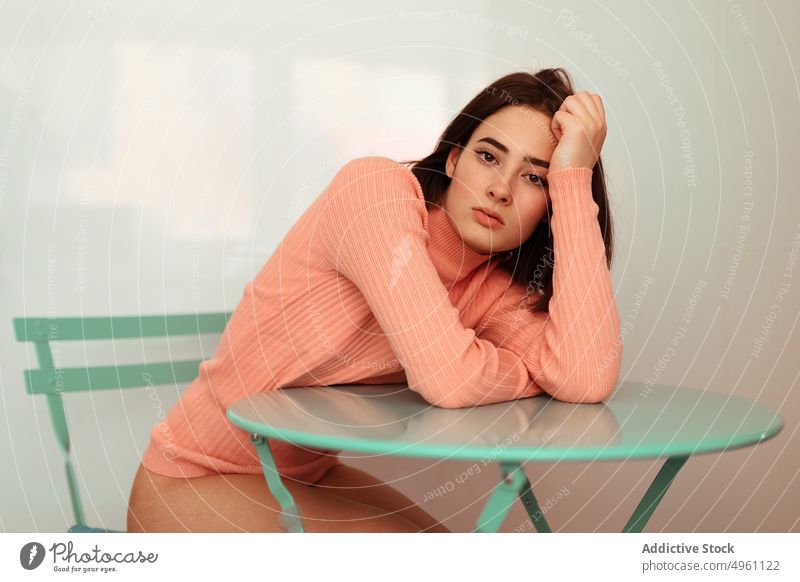 Serious woman leaning on table and looking at camera tranquil thoughtful sitting female adult thinking serious casual stylish lonely daydreaming pensive