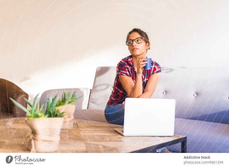 Thoughtful woman on sofa against assorted cacti in hotel pensive plant tropical exotic table thoughtful checkered ornament denim wear sit eyewear bun couch room