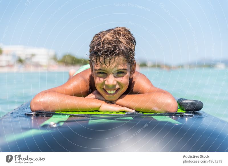Carefree boy lying on paddle board in sea paddleboard sup board summer relax teenage glad sunny vacation suntan clear delight holiday weekend carefree joy