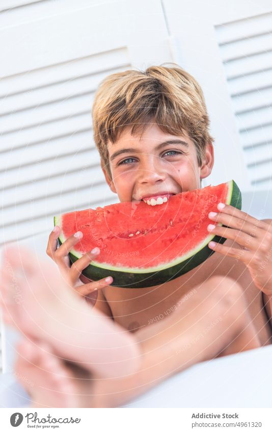 Cheerful boy eating juicy watermelon in summer enjoy juice ripe fresh happy teenage slice chair sit fruit tasty satisfied smile vacation summertime bite