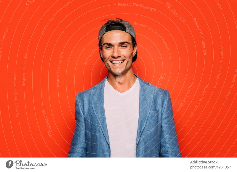 Stylish man with cap on red background fashion cool individuality make face stylish portrait modern having fun show gesture jacket trendy wear bright