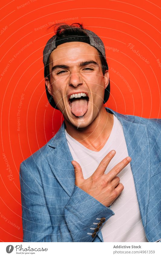Stylish man with tongue out on red background rap fashion cool individuality make face rude stylish portrait modern having fun show gesture jacket trendy wear