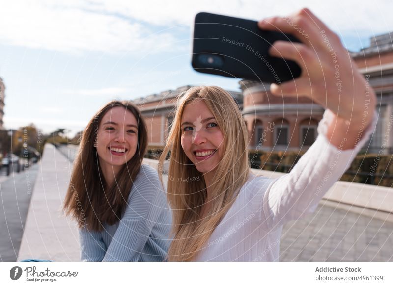 Positive women taking selfie on smartphone in city best friend cheerful having fun memory moment self portrait female madrid spain mobile together using smile