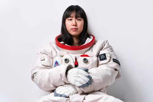 Asian cosmonaut looking at camera in studio woman break mission spacesuit wall lean portrait female young asian ethnic chinese japanese astronaut appearance
