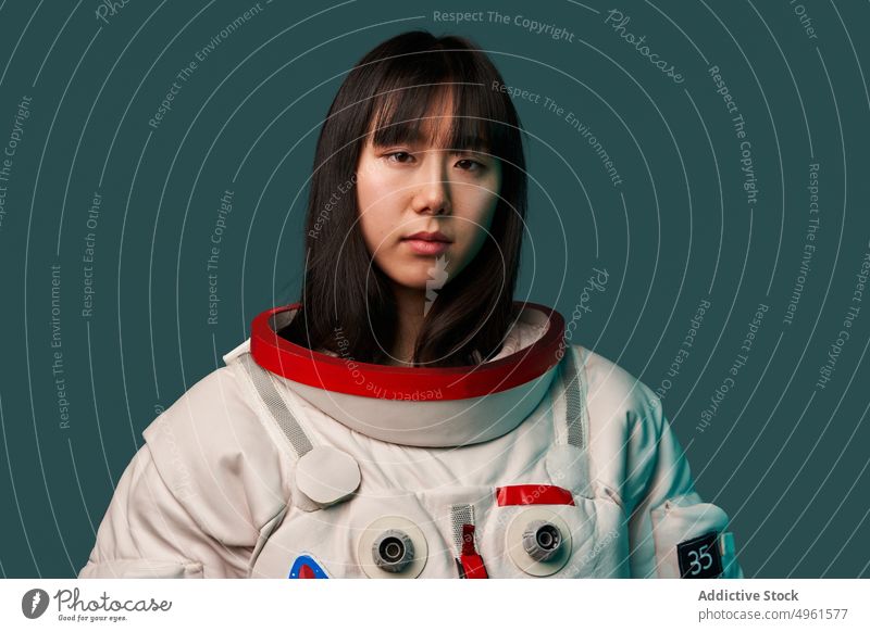 Calm Asian cosmonaut looking at camera woman ready mission calm serious spacesuit futuristic modern female young asian chinese japanese neon ethnic dark hair