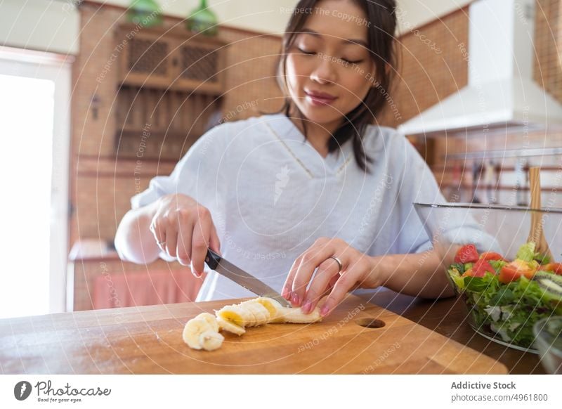 Asian woman slicing banana in kitchen cut cook salad home healthy food diet chopping board female asian ethnic fruit cutting board organic natural vegetarian