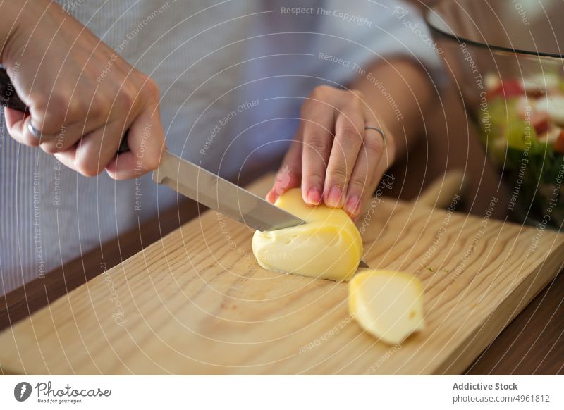 Crop woman cutting cheese on wooden board in kitchen cutting board food prepare cook culinary ingredient tasty meal female casual slice knife delicious dinner