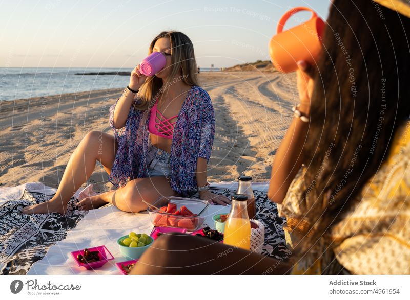 Diverse girlfriends drinking on beach women sea sunset picnic together weekend summer female blanket sip holiday multiethnic multiracial diverse black