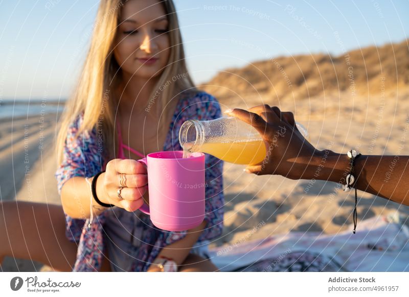 Anonymous black woman pouring juice for girlfriend women picnic beach summer together weekend drink female diverse multiracial multiethnic african american