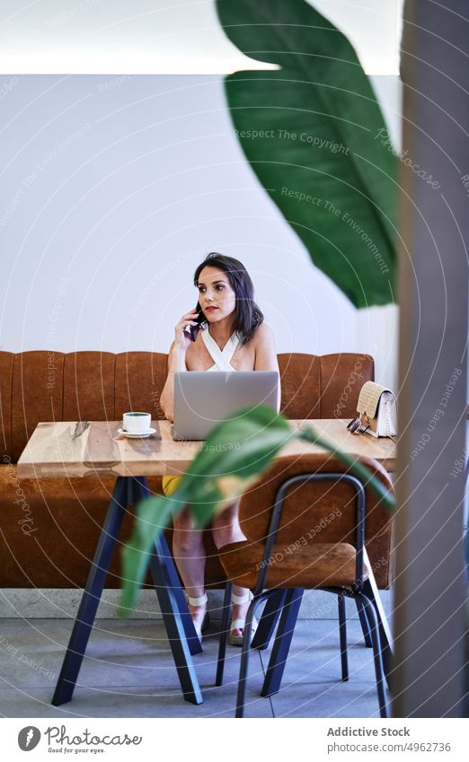 Businesswoman talking on smartphone and browsing laptop during work businesswoman project cafe multitask entrepreneur remote busy freelance mobile focus female