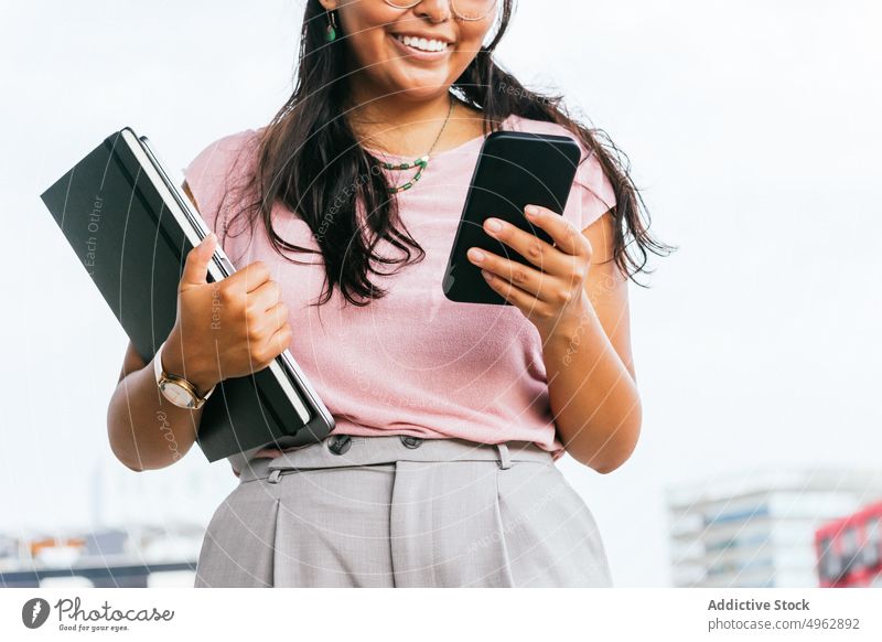 Smiling young ethnic businesswoman using smartphone near modern buildings message smile entrepreneur positive communicate internet street district female