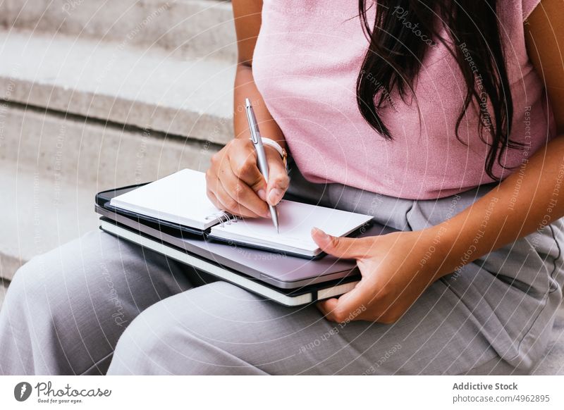 Crop unrecognizable lady taking notes in jotter sitting on stairs on street woman take note notebook freelance write laptop schedule work planner remote female