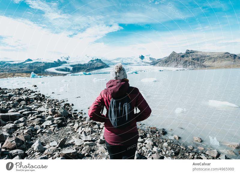 Solo female in rain clothes in front of the Jokulsarlon glacier. Back shot, during a road trip travel exploring wild lands of Iceland.Adventure vacations healthy lifestyle backpacking
