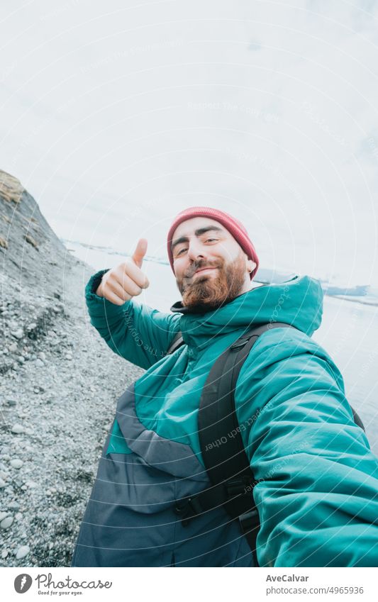 Solo male traveler on Iceland happy bout road trip new experiences. Living freedom and explore backpacking. Bearded hipster handsome guy doing the all good sign to camera taking a selfie while hiking.