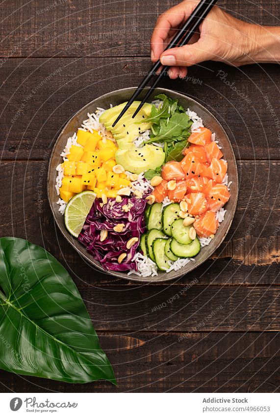 Anonymous person eating poke bowl with assorted veggies rice and salmon avocado mango asian food chopstick healthy food cucumber dish cuisine fish meal
