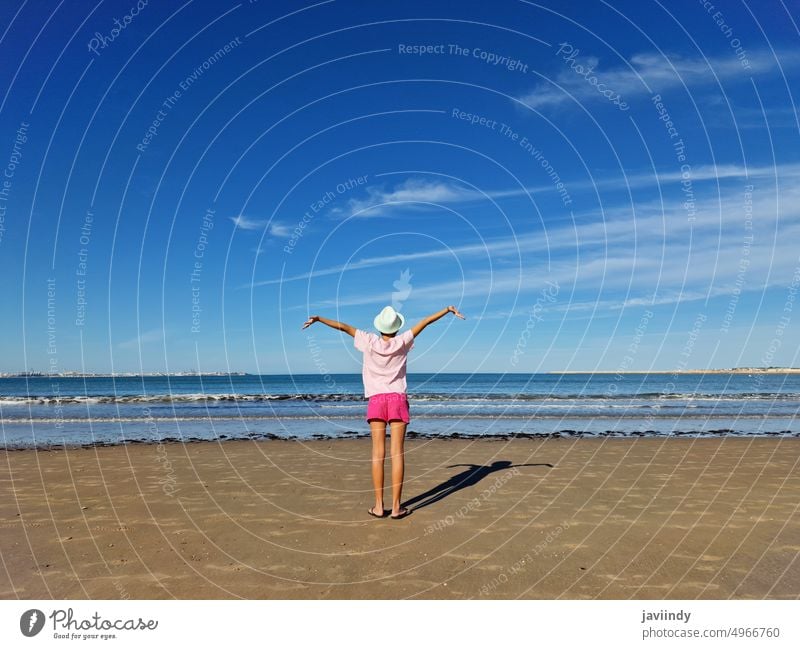 Girl with hat opening her arms in front of the sea, on a sandy beach. child girl summer back baby relax water person kid nature vacation ocean tropical