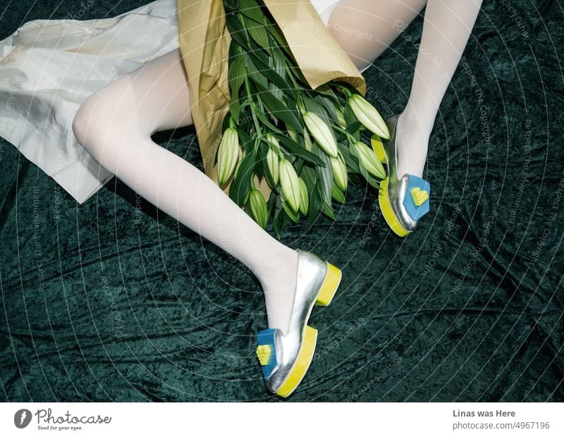 An image of some nice shiny shoes and a girl wearing them. Lying on cashmere and holding a bouquet of lilies. An avant-garde women's shoe fashion that looks splendidly.