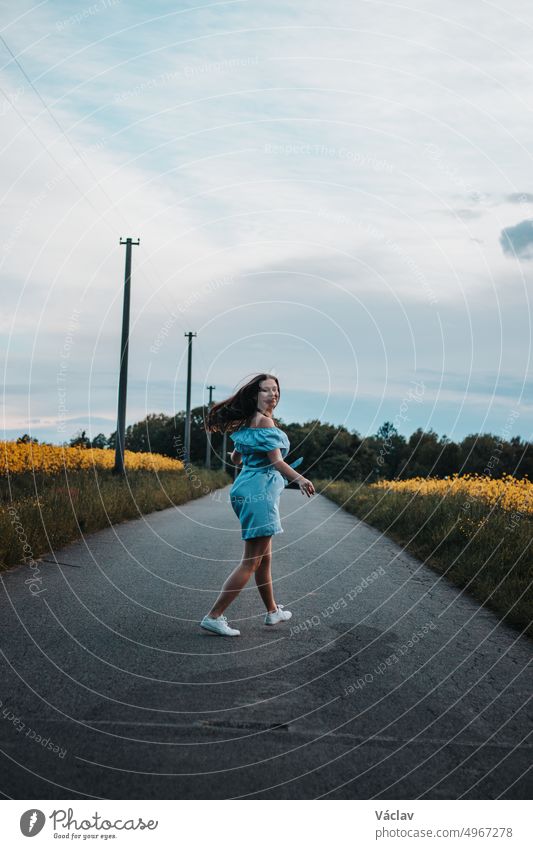 Young 20-24 year old slim brunette in a light blue summer dress dances on the road to the rhythm of the music. Candid portrait of a real ordinary person enjoying movement and dancing. Knowing oneself