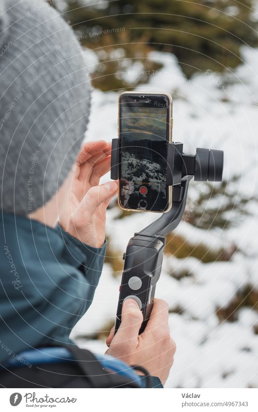 young yutuber vlogs on his social networks using a mobile phone and a gimbal for better video. Winter recording. Athlete. Detail on video transmission. Video settings