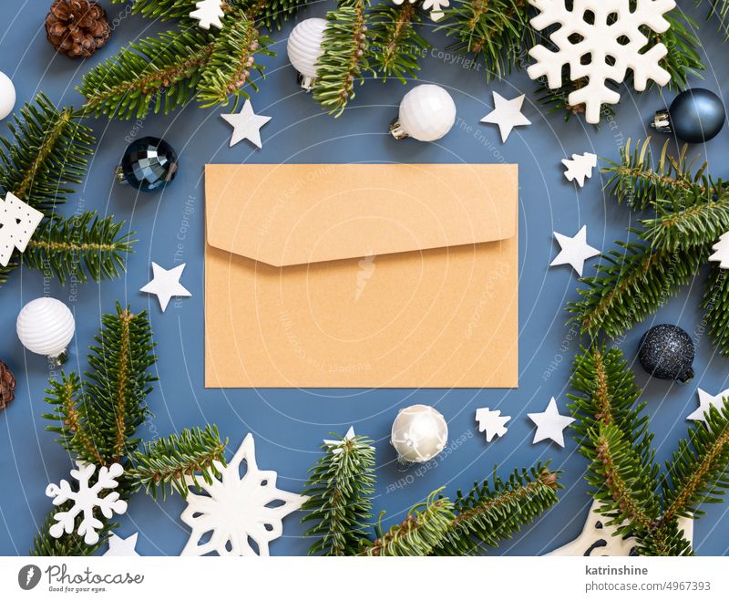 Craft paper envelope on a blue background near white Christmas decorations and fir branches mockup ornaments blank copy space craft kraft new Year top view