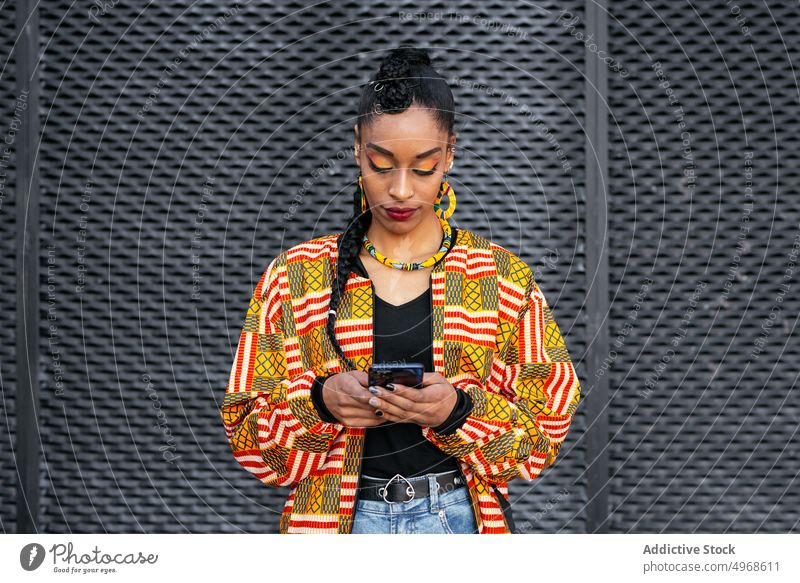 Stylish woman using smartphone on street style wall urban female young ethnic modern browsing trendy online internet colorful surfing app shirt scroll braid