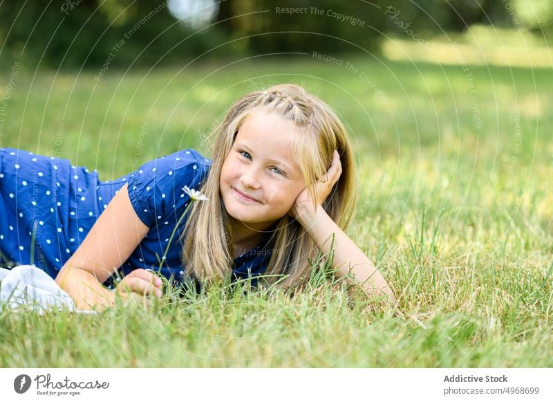 Happy girl lying on grass field rest smile flower daisy weekend summer happy lean on hand blond lawn meadow bloom glad blossom flora child cheerful positive