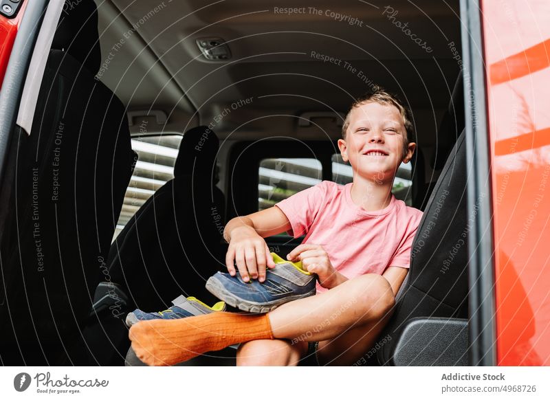 Smiling boy putting on shoe on back seat put on car backseat fasten road trip cheerful weekend glad prepare happy passenger kid smile vehicle casual auto