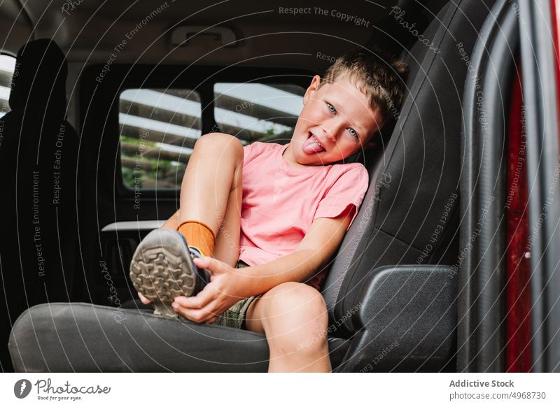 Smiling boy putting on shoe on back seat put on car backseat fasten road trip cheerful weekend glad prepare happy passenger kid smile vehicle casual auto