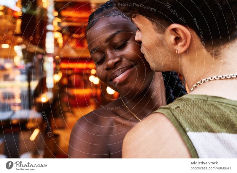 Man kissing black girlfriend near restaurant couple date love street happy romantic affection relationship smile cheek eyes closed boyfriend young