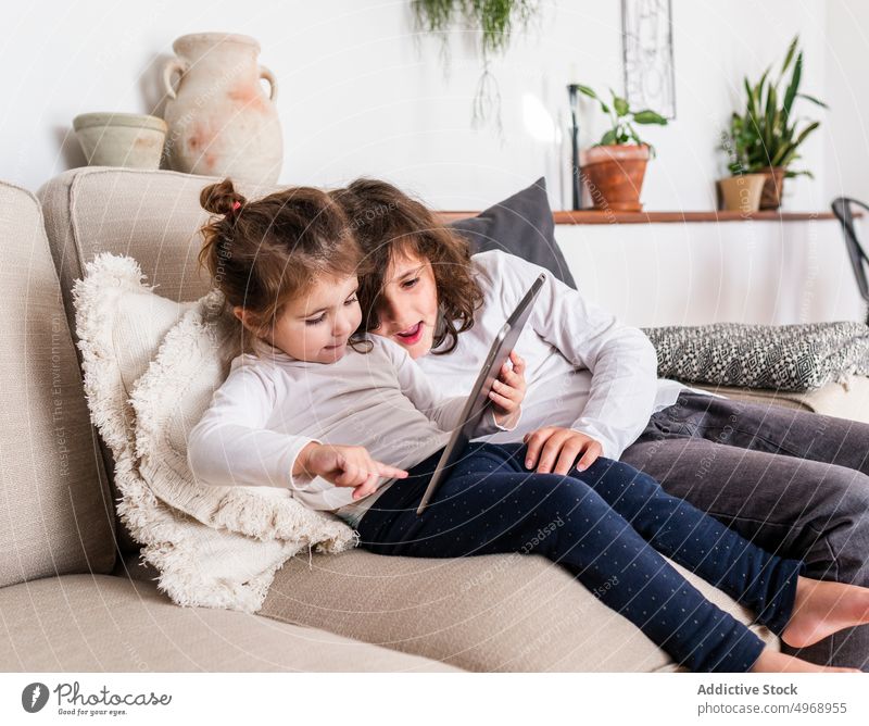 Children using tablet on sofa girl children device apartment together sister childhood home kid comfort gadget adorable lying light cute rest relax couch
