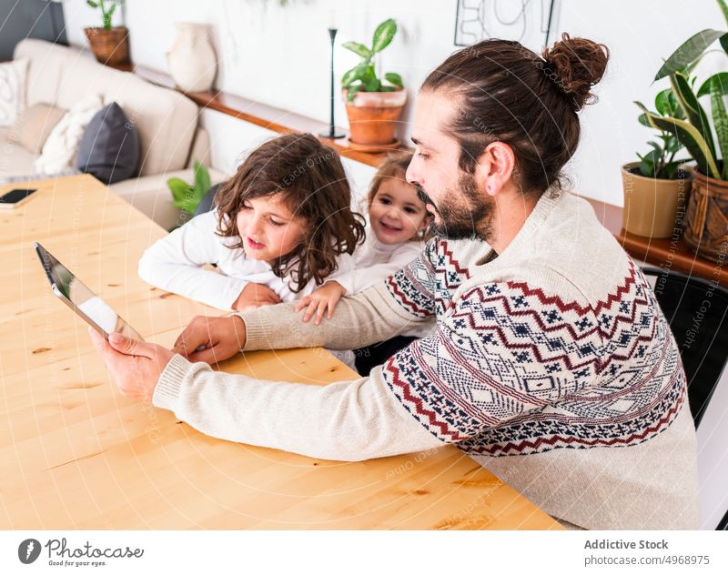 Man and children using tablet man father together relationship apartment device happy male girl kid wooden sit smile home beard gadget warm sweater parent