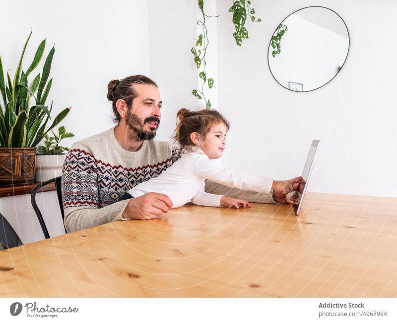 Father with daughter at home browsing on tablet man girl apartment together child modern cheek male father device gadget using relationship beard parent sit