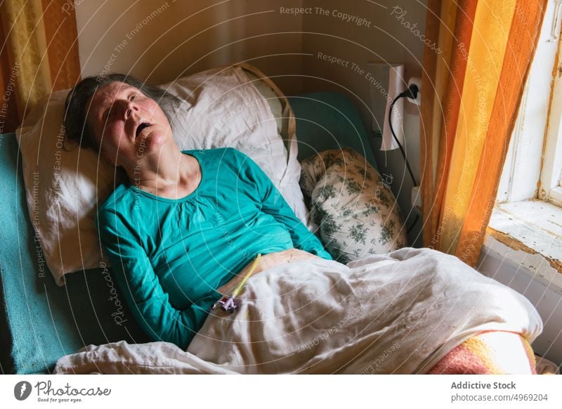 Paralyzed elderly lady lying on bed at home woman paralyzed medical room disability care patient female senior mature pensioner support assistance handicapped