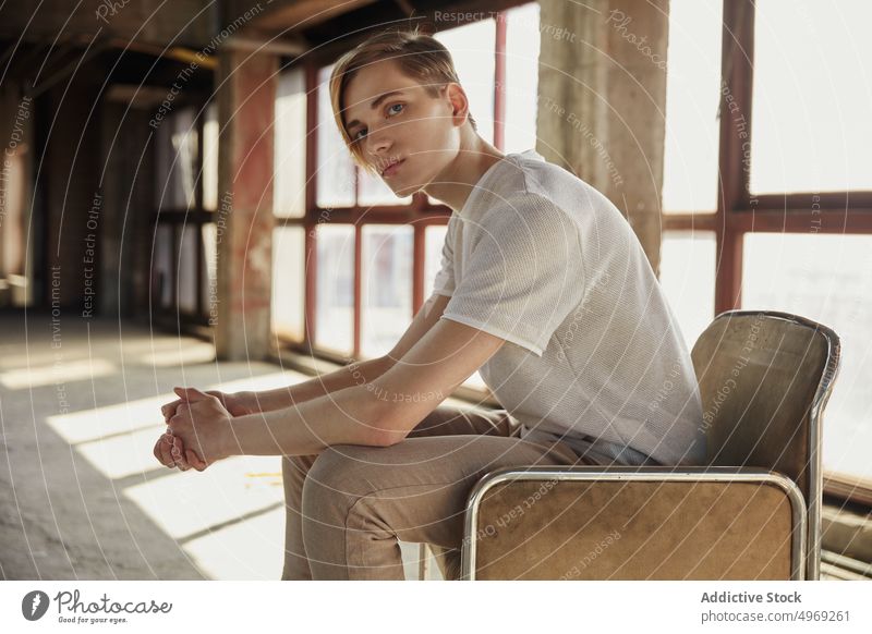 Young trendy man sitting on chair in hall empty handsome relaxed urban glamour cool elegance stylish confidence vogue model young male guy attractive happy