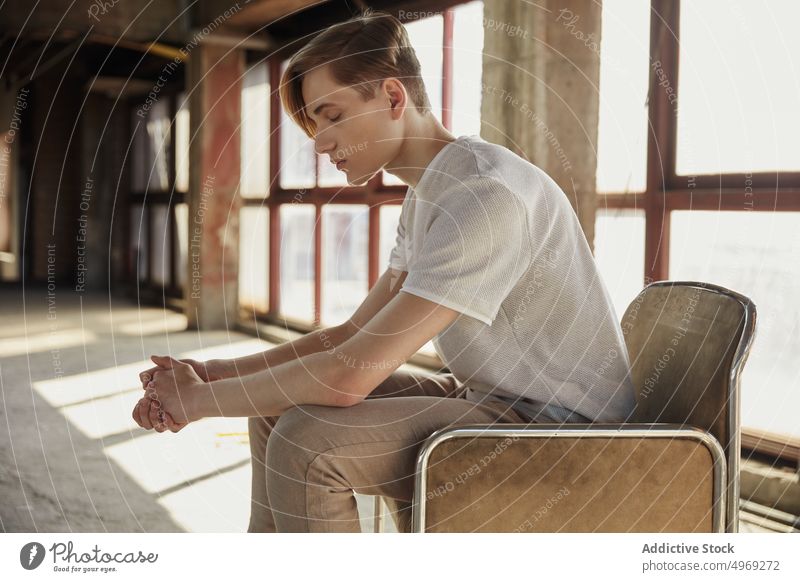 Young trendy man sitting on chair in hall empty handsome relaxed urban glamour cool elegance stylish confidence vogue model young male guy attractive happy
