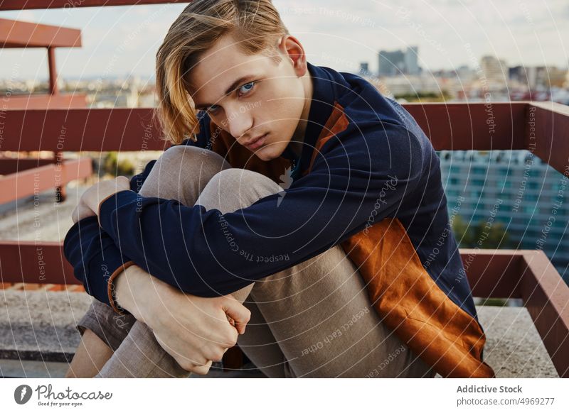 Young blond male sitting on roof of building man handsome relaxed urban trendy stylish model vogue young glamour cool elegance guy confidence attractive happy