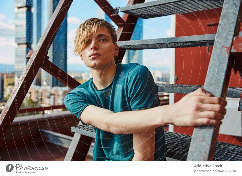 Fashionable young man sitting on ladder on roof handsome relaxed urban trendy stylish model cool male guy attractive happy city serious confident mature