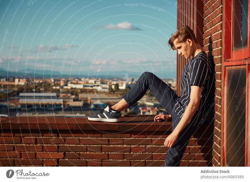 Handsome young male sitting on roof man building street handsome relaxed urban trendy stylish model summer blond attractive happy serious mature fashionable