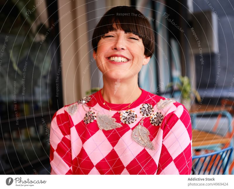 Positive woman with toothy smile on terrace of summer cafe cheerful trendy content classy hairstyle bob female outfit modern joy enjoy urban street apparel wear