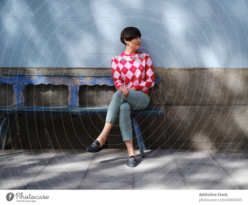 Woman in trendy outfit relaxing on bench in city woman classy style hairstyle bob shabby female wooden calm street rest building sit exterior urban peaceful