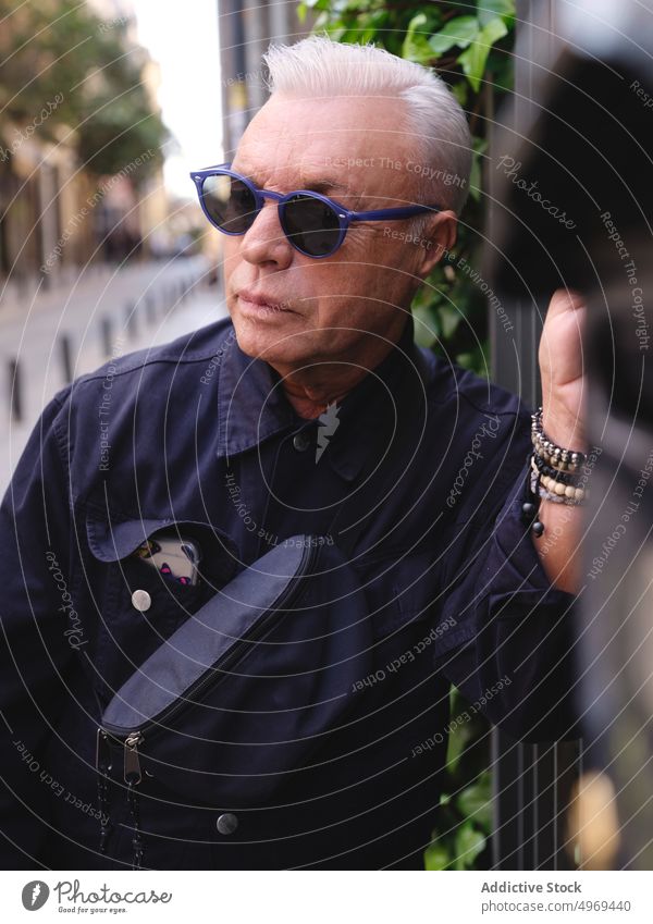 Fashionable senior man with belt bag on street fashion trendy confident aged style urban male metal fence shirt sunglasses city serious handsome relax stand