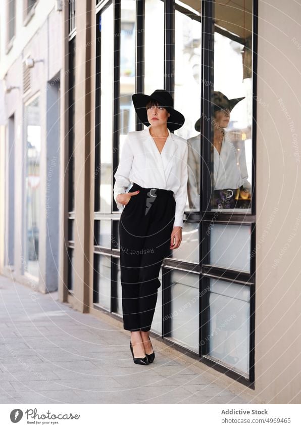 Elegant woman in hat in city charming elegant street style trendy female high heels building urban lady fashion beauty short hair stand lean glass wall outfit