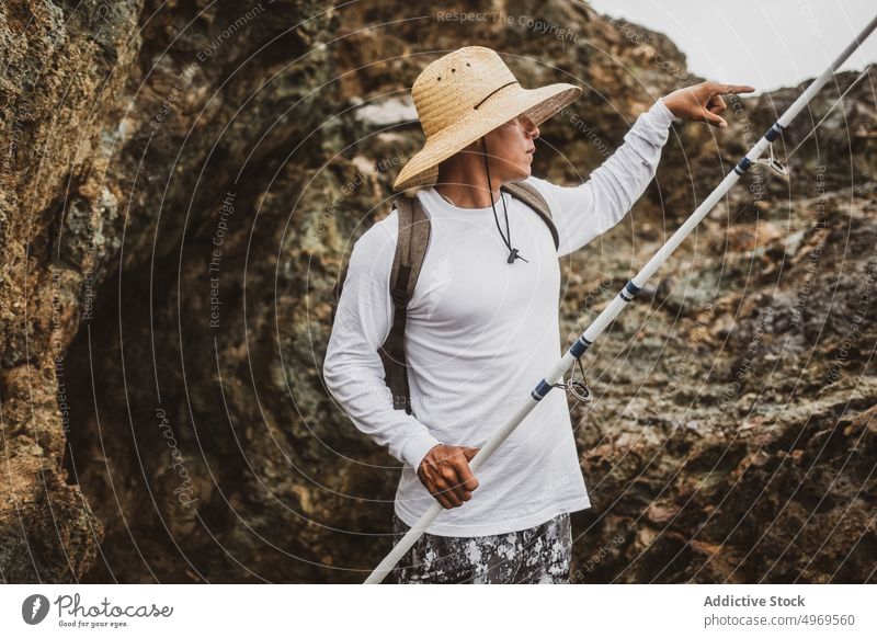 Anonymous fisherman with rod near cliff fishing coast shore hobby equipment seashore leisure mountain rock male seaside hat angler skill lifestyle rest