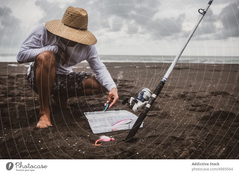 Unrecognizable fisherman choosing fishing lures on seashore - a
