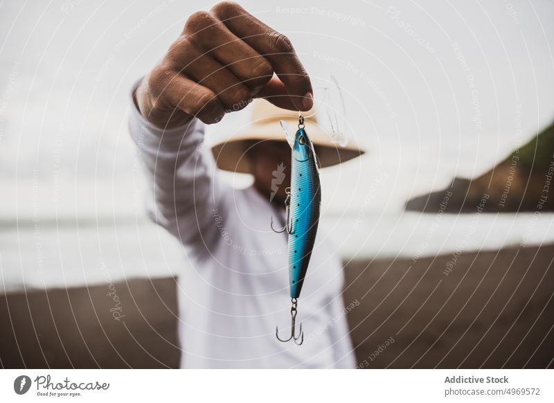 Unrecognizable fisherman with plug in hand blue fishing tackle lure coast shore supply hobby equipment prepare male seashore seaside hat angler skill lifestyle