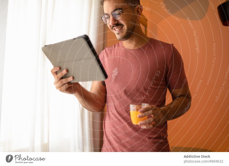 Positive man with tablet and juice internet online beverage room hotel browsing pastime gadget device using cellphone glass thirst window male surfing content