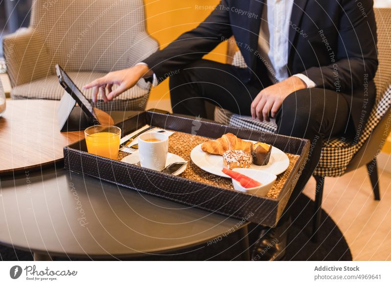 Unrecognizable man using tablet at table with tray of food entrepreneur online dessert coffee hotel browsing serve male device morning lunch business trip